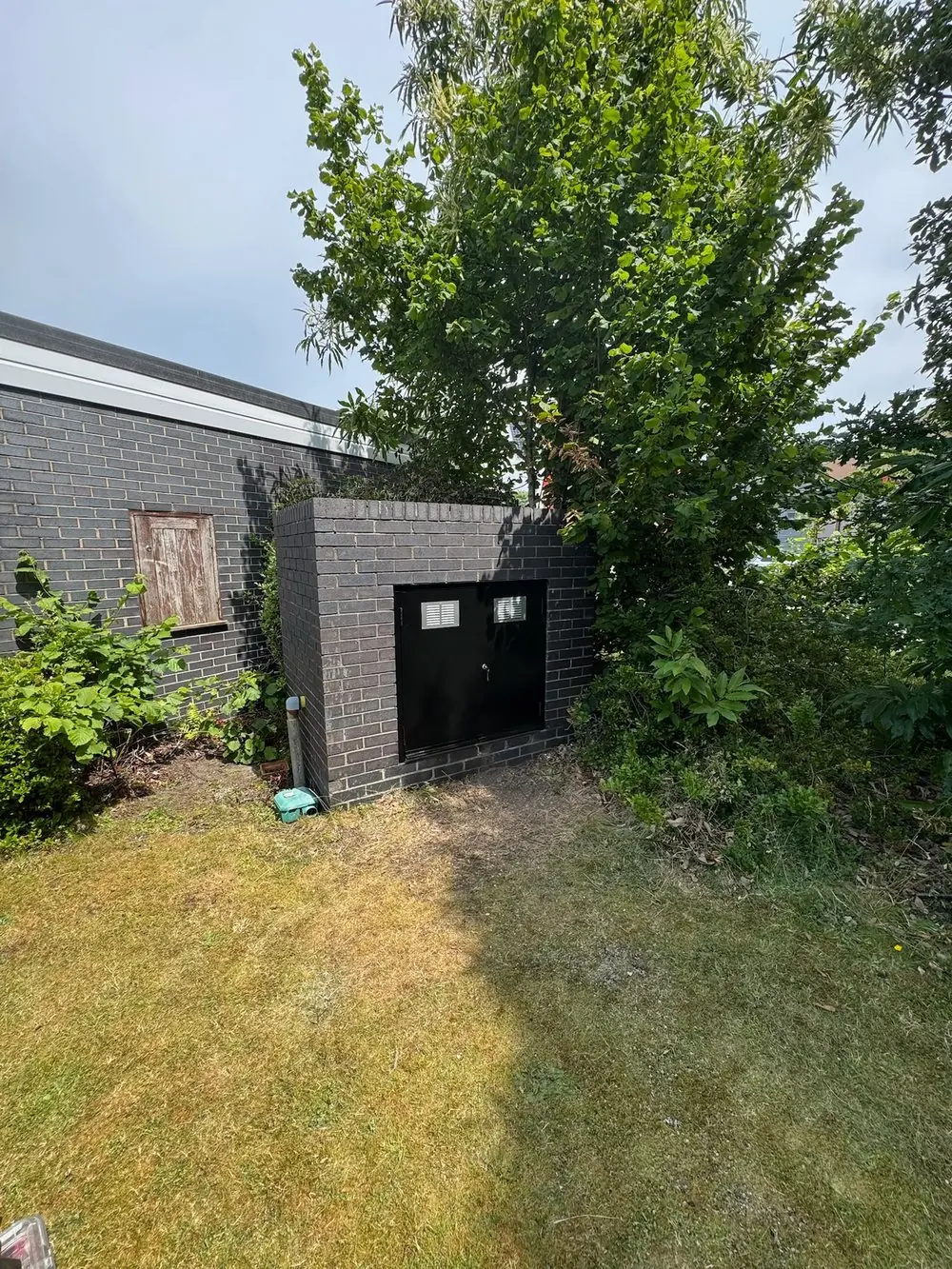 Gas meter enclosure tucked into the planting beside the building